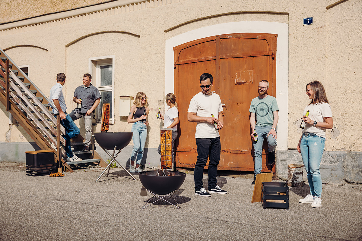Flame-grilled salmon board Depicted here is a group of people standing around a fire pit, with the Flame-grilled salmon board.