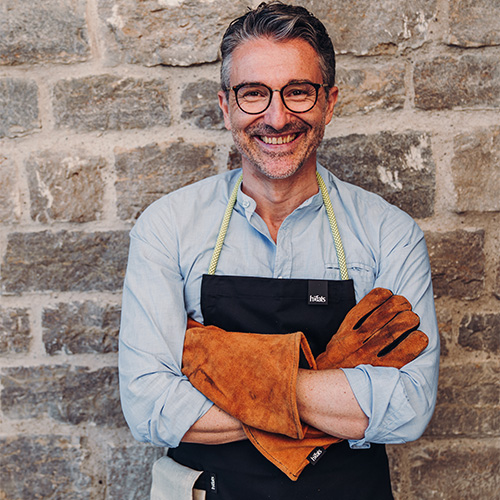 The photo presents a man wearing a black apron