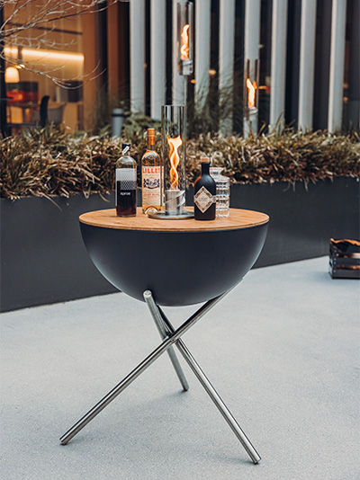 The photo presents a table with a bottle of wine on it, with the BOWL Fire Bowl.