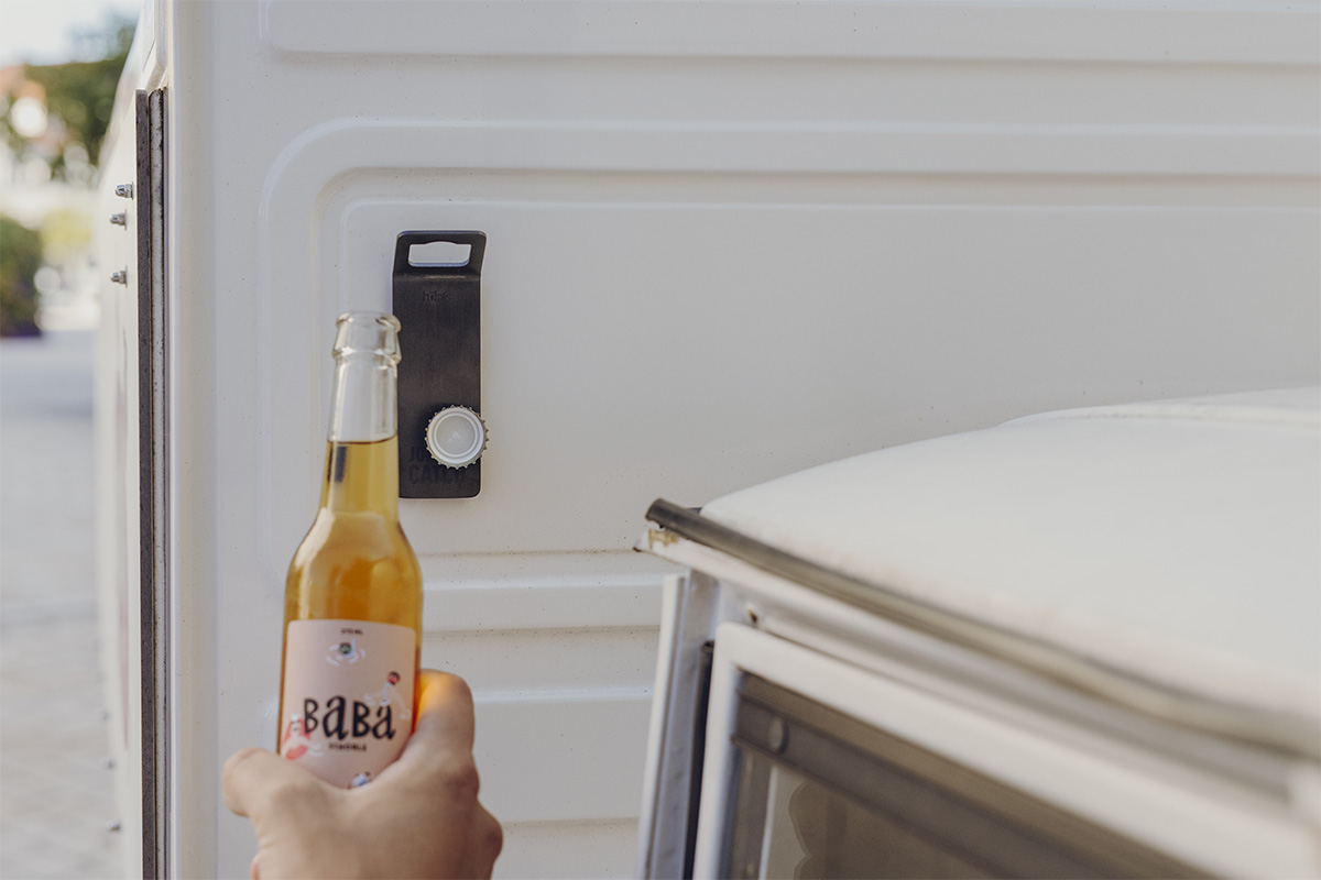 A person opening a drink with a wall mounted bottle opener, with the 00841 Johnny Catch Magnet Black Bottleopener adding a functional and elegant touch to the scene.