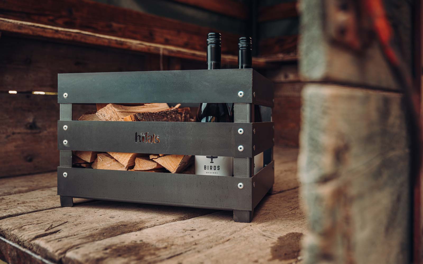 A metal crate with a bottle of wine in it, enriched by the presence of the Crate Firebasket, which merges design with utility.