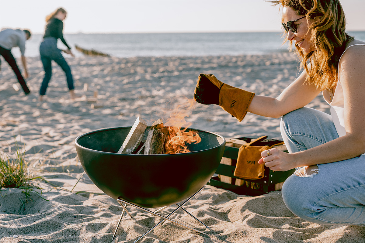 A depiction of a woman sitting on the beach, featuring the 00249 Bowl 57 with star stand as a central and purposeful element.