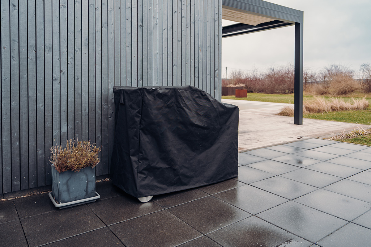 A depiction of a black predective cover sitting on a patio, featuring the 00826 Fire Kitchen Cover 57 as a central and purposeful element.