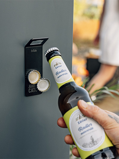 A person opening a bottle of beer from a bottle opener. the Johnny Catch Magnet Bottleopener complements the moment with its thoughtful design.