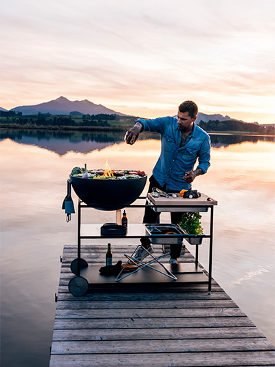 Scene showing a man cooking on a dock, where the Fire Kitchen stands out for its practical elegance.