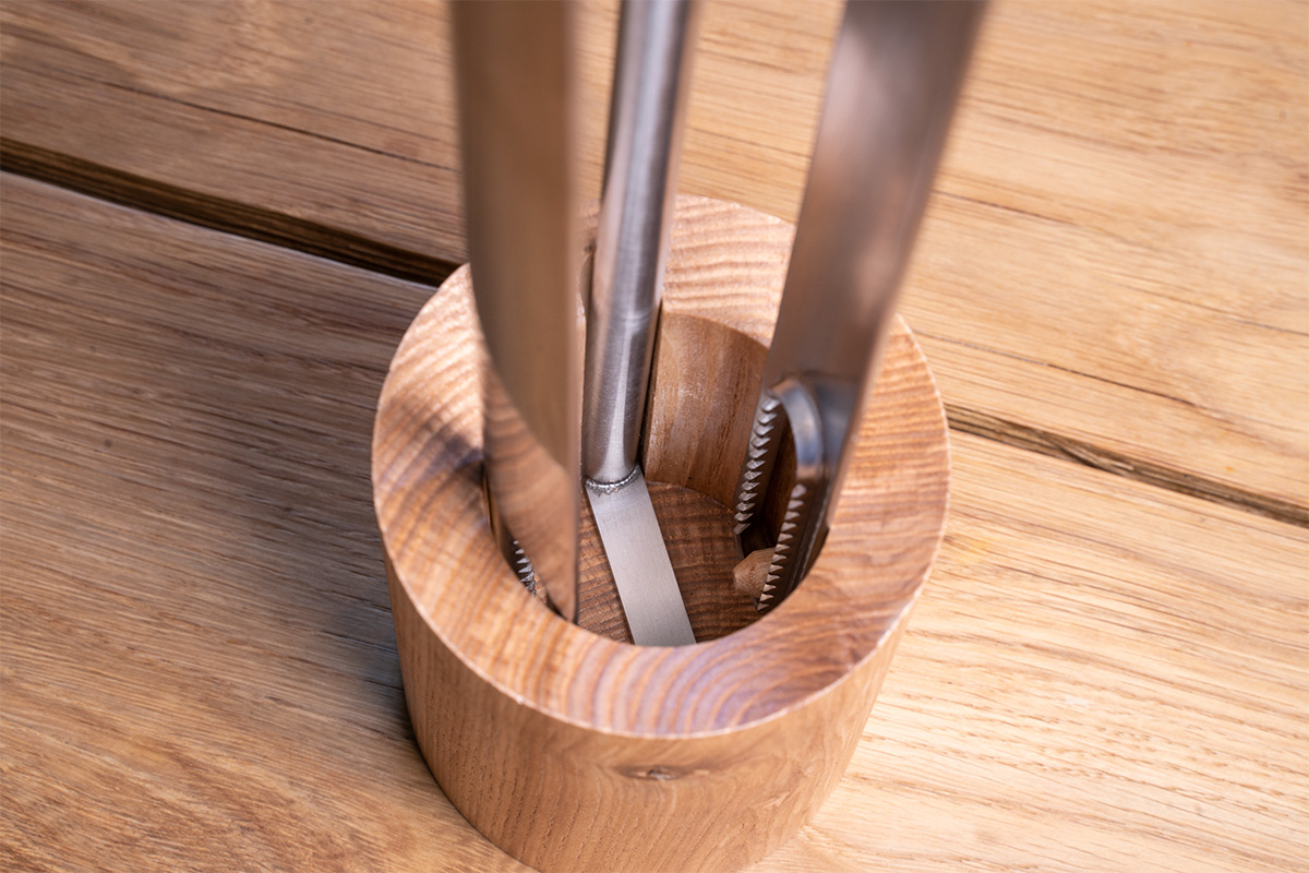 A tong in a wooden holder on a table, enriched by the presence of the 00251 Fire Tools Set 3 pcs, which merges design with utility.