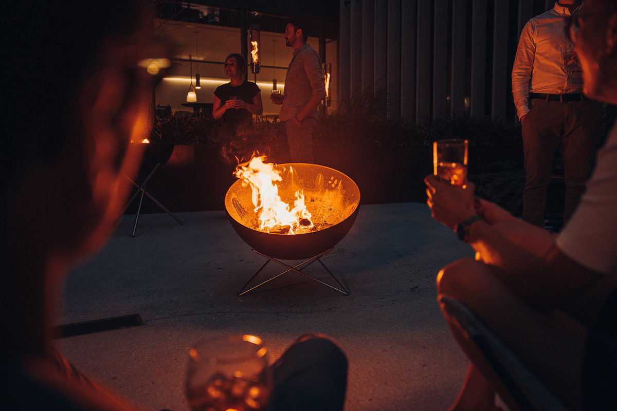 BOWL 70 Fire Bowl with star stand A view of a group of people sitting around a fire pit, with the BOWL 70 Fire Bowl with star stand.