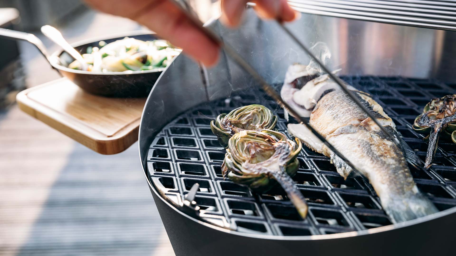 The photo presents a person is cooking fish on a grill, with the CONE.