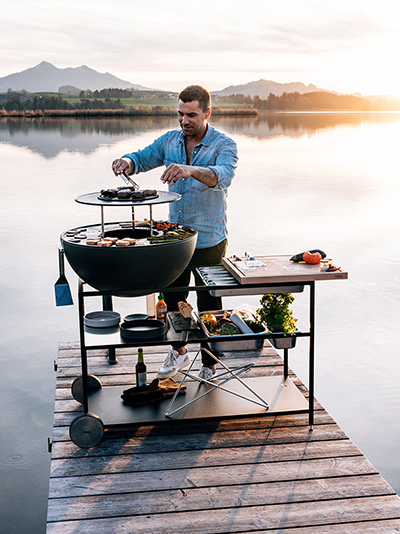 A view of a man grilling on a wooden dock, with the BOWL 70 Sear Grate.