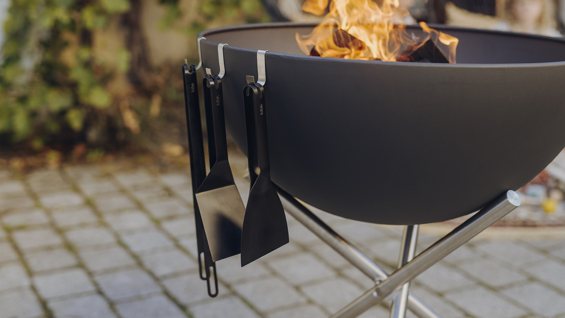 An inviting scene with a fire pit with a fire in it, highlighted by the presence of the 00878 Bbq Tool Set black