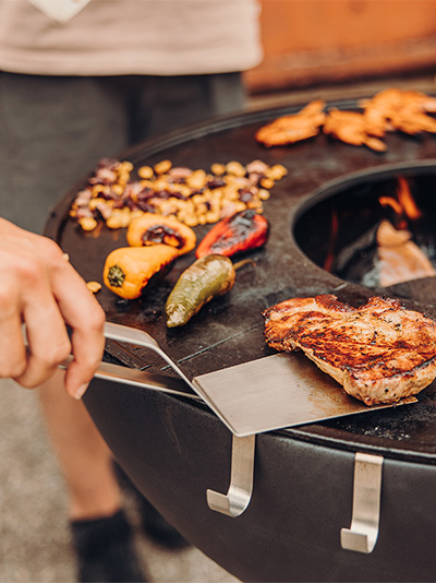 A depiction of a person is cooking food on a grill, featuring the 00473 Spatula as a central and purposeful element.