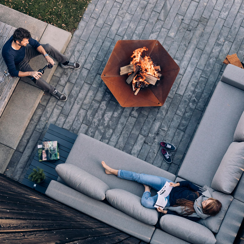 A depiction of a group of people sitting around a fire pit, featuring the Triple Fireplace as a central and purposeful element.