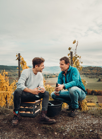 Illustrated is two men sitting on a hill in the fall, with the CRATE Fire Basket.