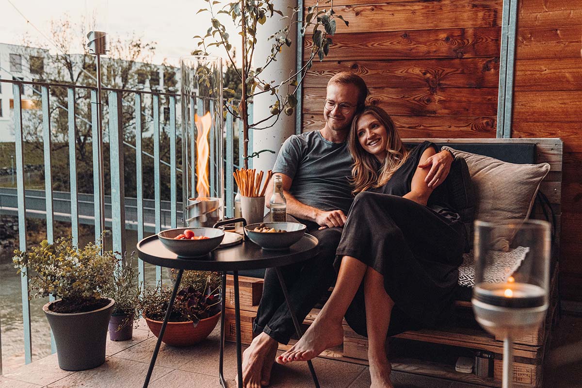 Scene showing a man and woman sitting on a couch with a plate of food, where the Spin 90 Tablefire silver stands out for its practical elegance.