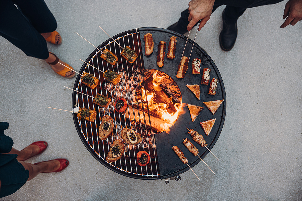 An image showing a group of people standing around a grill, with the .
