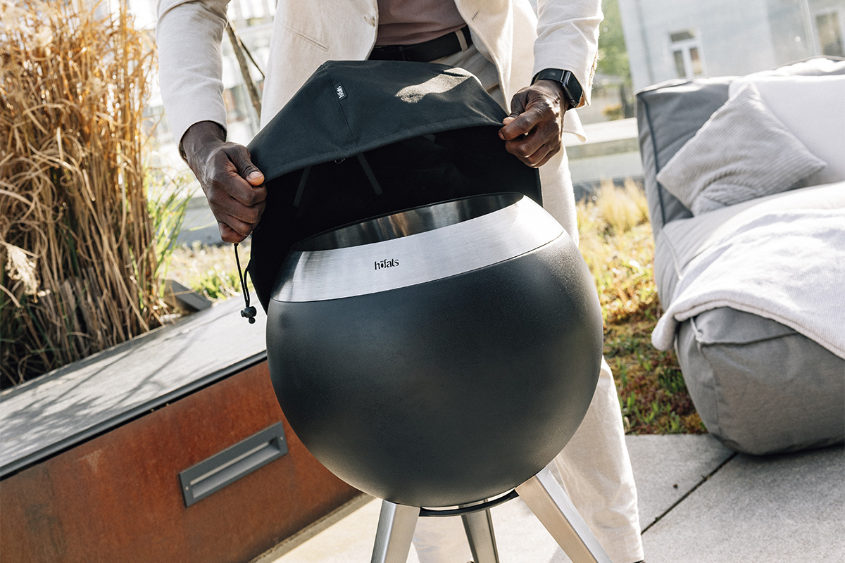 MOON 45 Cover A man holding a large black cover over a firebasket, with the 00815 Moon 45 Cover adding a functional and elegant touch to the scene.