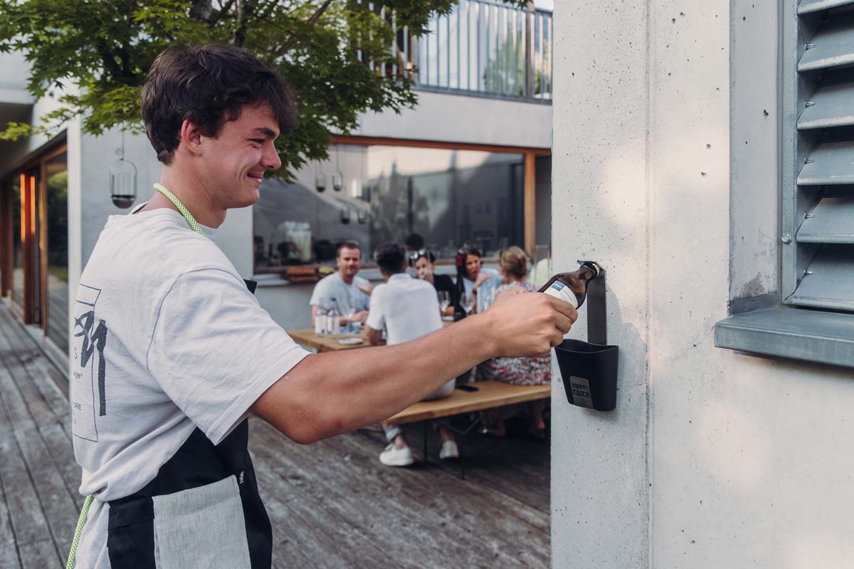 A depiction of a man opening a bottle at a restaurant, featuring the Johnny Catch Cup Bottle opener as a central and purposeful element.