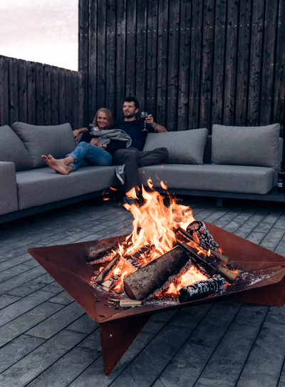 The Triple Fireplace integrates seamlessly into the setting, where a man sitting on a couch next to a fire pit.