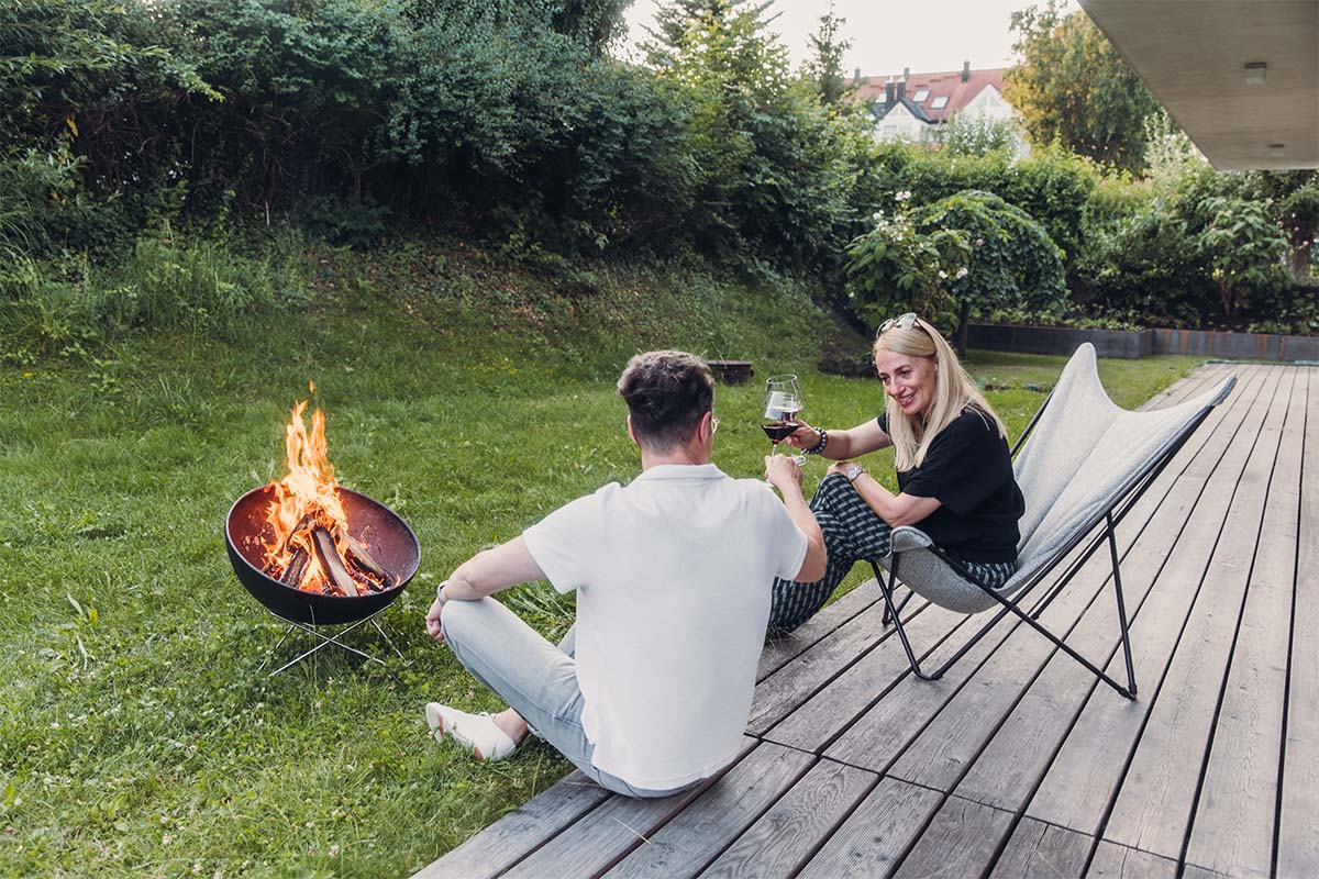 BOWL 57 Star stand An inviting scene with a man and woman sitting on a bench next to a fire pit, highlighted by the presence of the 00343 Bowl 57 Star Stand