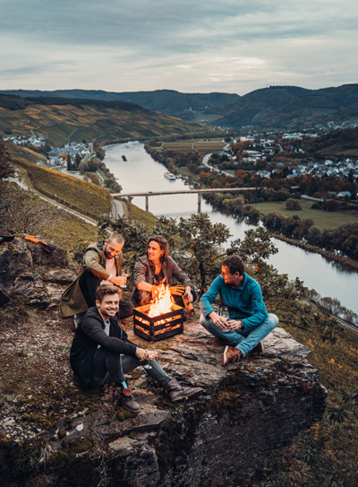 The photo presents a group of people sitting around a campfire, with the CRATE Fire Basket.