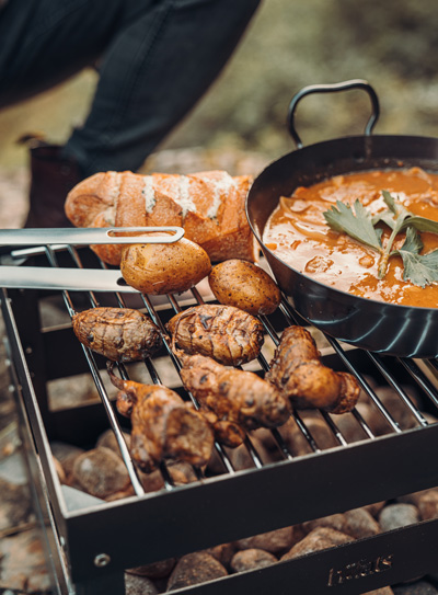 A person is cooking food on a grill the Crate Firebasket complements the moment with its thoughtful design.