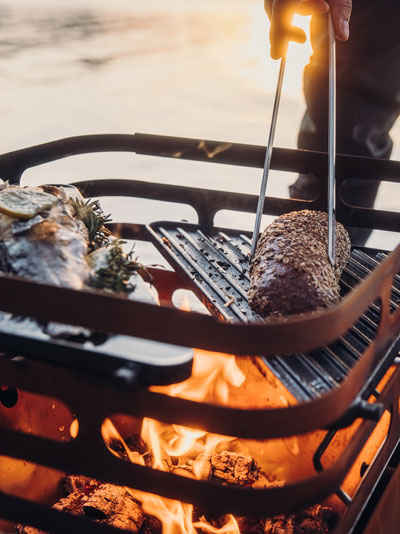 A man grilling meat on a grill the Cube Firebasket with Plancha complements the moment with its thoughtful design.