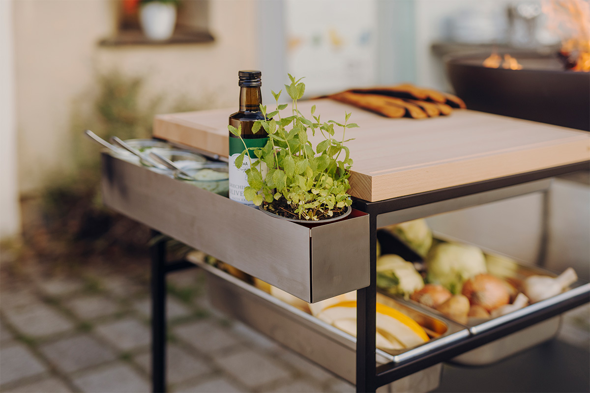 A metal frame with a bottle of oil and a tray of food, the 00830 Fire Kitchen Tool Box complements the moment with its thoughtful design.