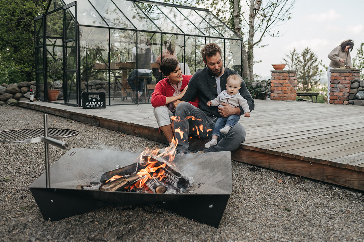 A view of a man and woman sitting around a fire pit, with the TRIPLE 120 Fire Bowl.