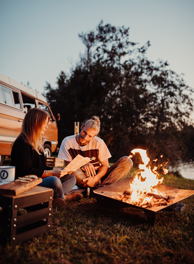 A couple sitting around a camper van on a camping trip, enriched by the presence of the Triple Fireplace, which merges design with utility.