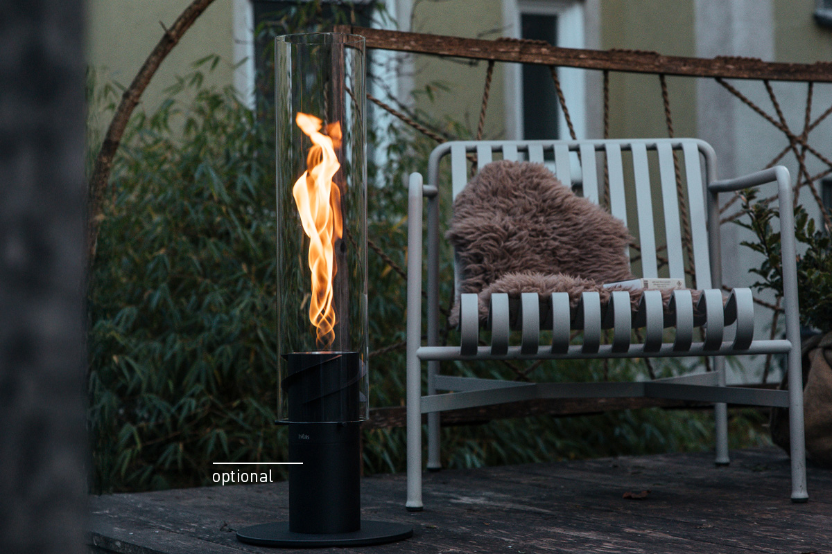 SPIN 1500 Pedestal Fireplace black A fire is burning in a SPIN Tablefire, outside next to a cozy chair, with the 00628 Spin 1500 Tablefire black adding a functional and elegant touch to the scene.