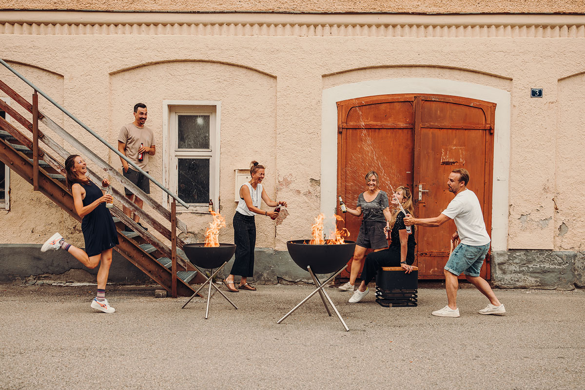 BOWL 70 Tripod The photo presents a group of people sitting around a fire pit, with the BOWL 70 Tripod.