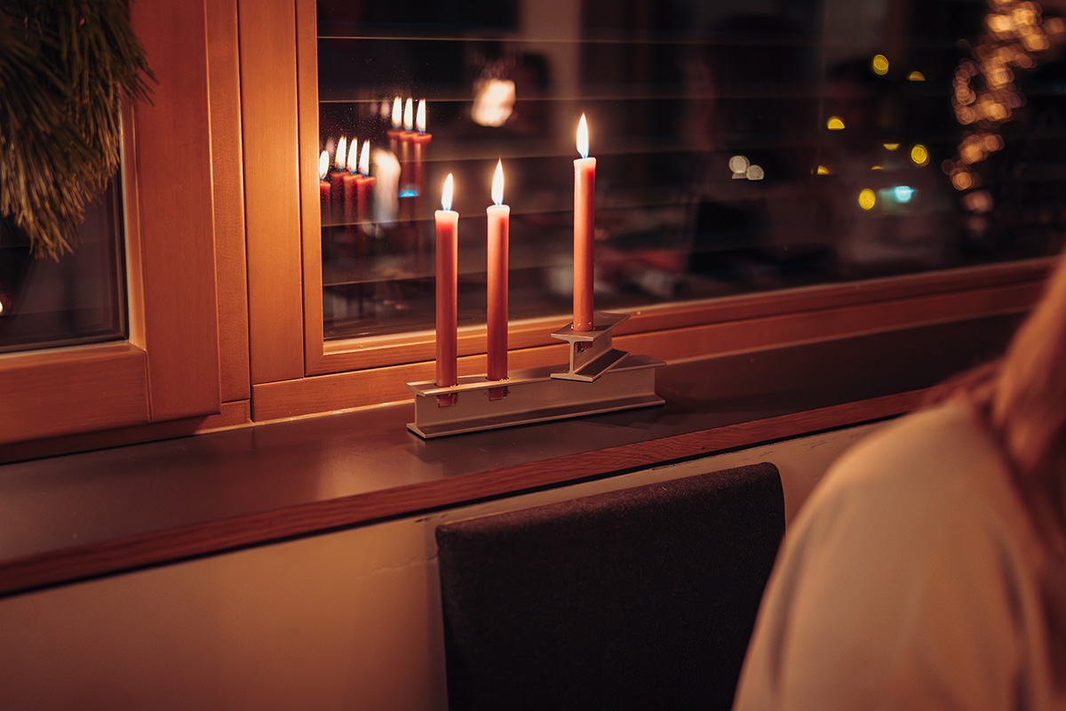 A woman sitting in front of a window with a lit candle the 00798 Henry Metal I and II silver complements the moment with its thoughtful design.