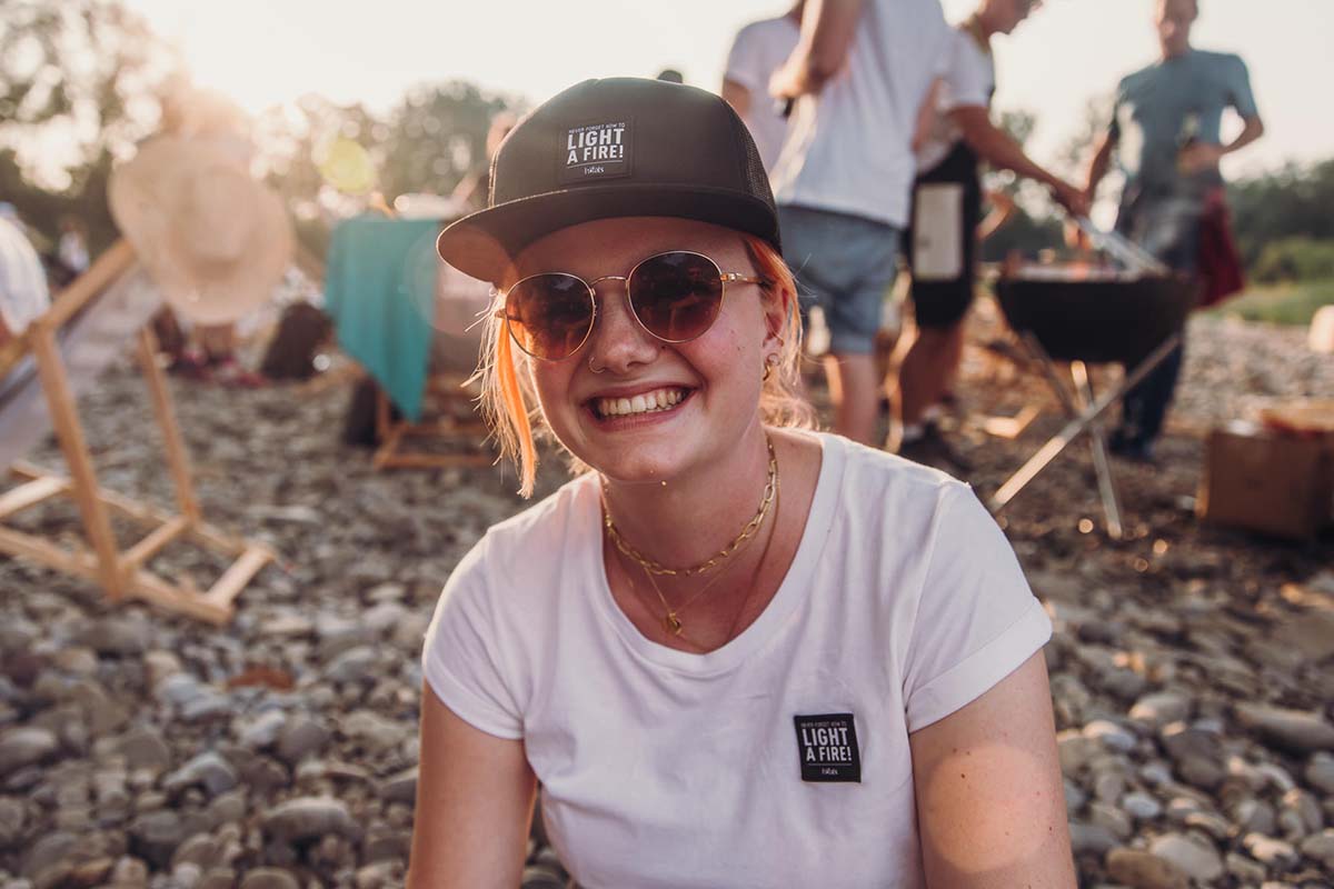 a woman wearing a hat and sunglasses sits on rocks.
