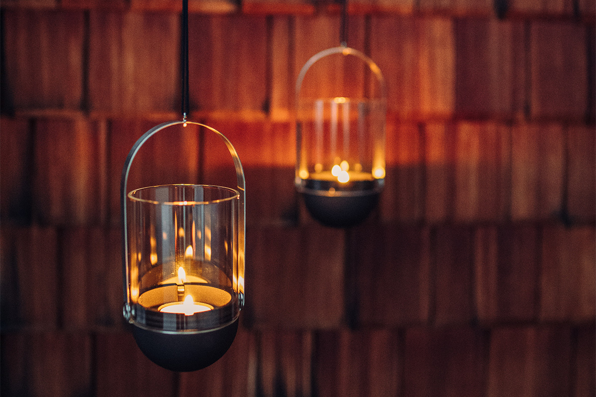 The photo presents a couple of hanging candles on a wall, with the GRAVITY CANDLE Lantern black.