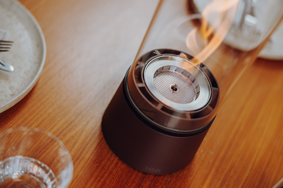 SPIN air 900 Tabletop Fireplace oxyde red SPIN air 1200 rostbraun an einem runden Tisch mit Tellern und Menschen Close-Up