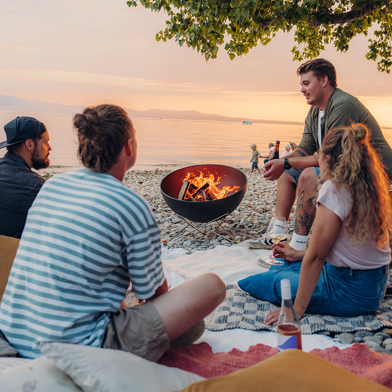 A group of people sitting around a fire pit, with the Bowl 57 with starstand adding a functional and elegant touch to the scene.