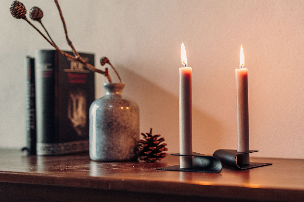 The photo presents a couple of candles sitting on a table, with the SQUARE CANDLE Candleholder black.