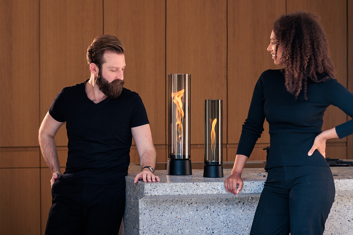 SPIN air 1200 Tabletop Fireplace all black Zwei Personen lehen an Tisch und schauen in die Flamme von SPIN air 900 mattschwarz und SPIN air 1200 mattschwarz