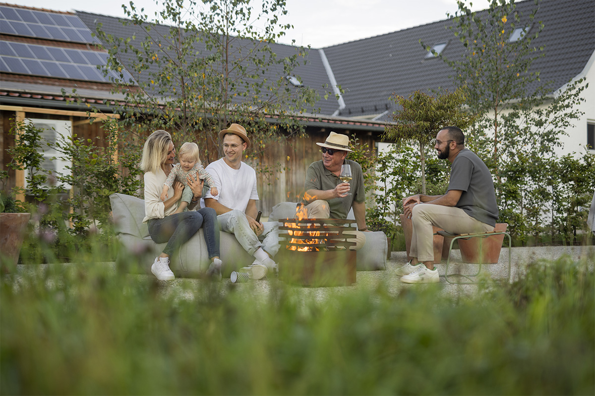 CUBE Fire Basket Corten Steel A group of people sitting around a fire pit, with the Cube Firebasket Rusty adding a functional and elegant touch to the scene.