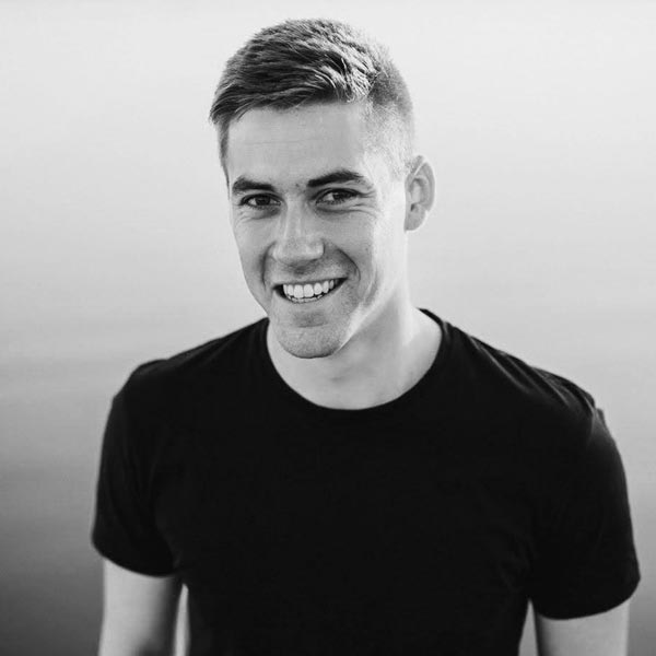 a man smiling while standing in front of a lake.