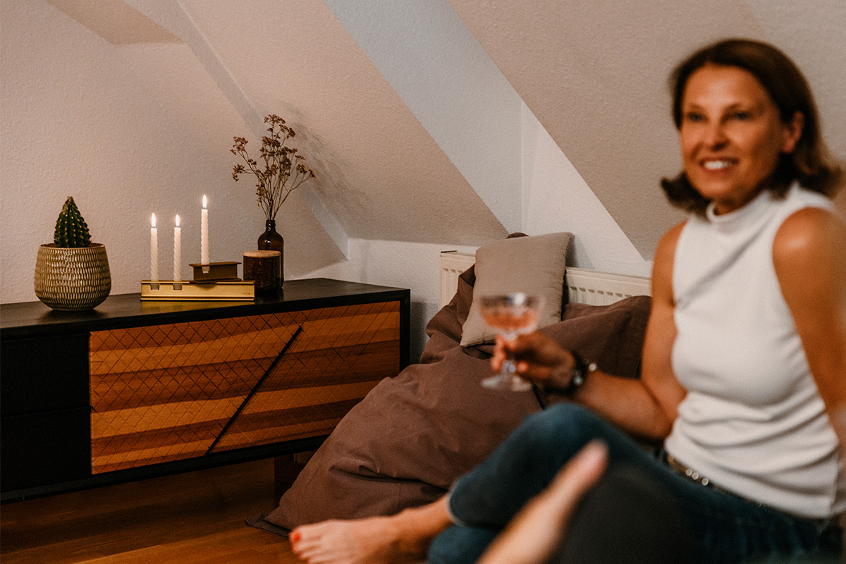 HENRY METAL II Candleholder gold Scene showing a woman sitting on a couch holding a glass of wine, where the 00662 Henry Metal II Gold stands out for its practical elegance.