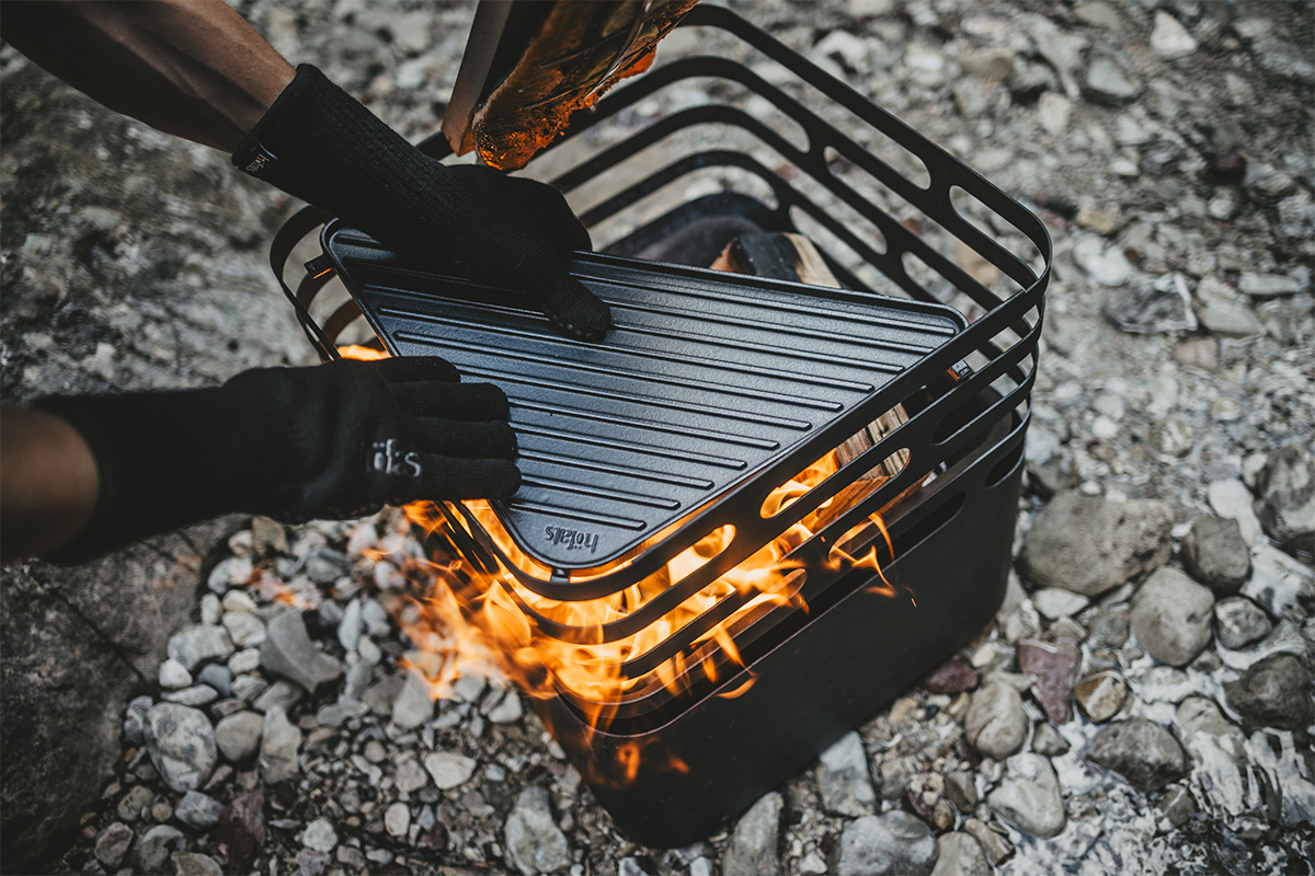 Scene showing a person is cooking on a grill, where the 00715 Feuerhandschuhe Aramid stands out for its practical elegance.