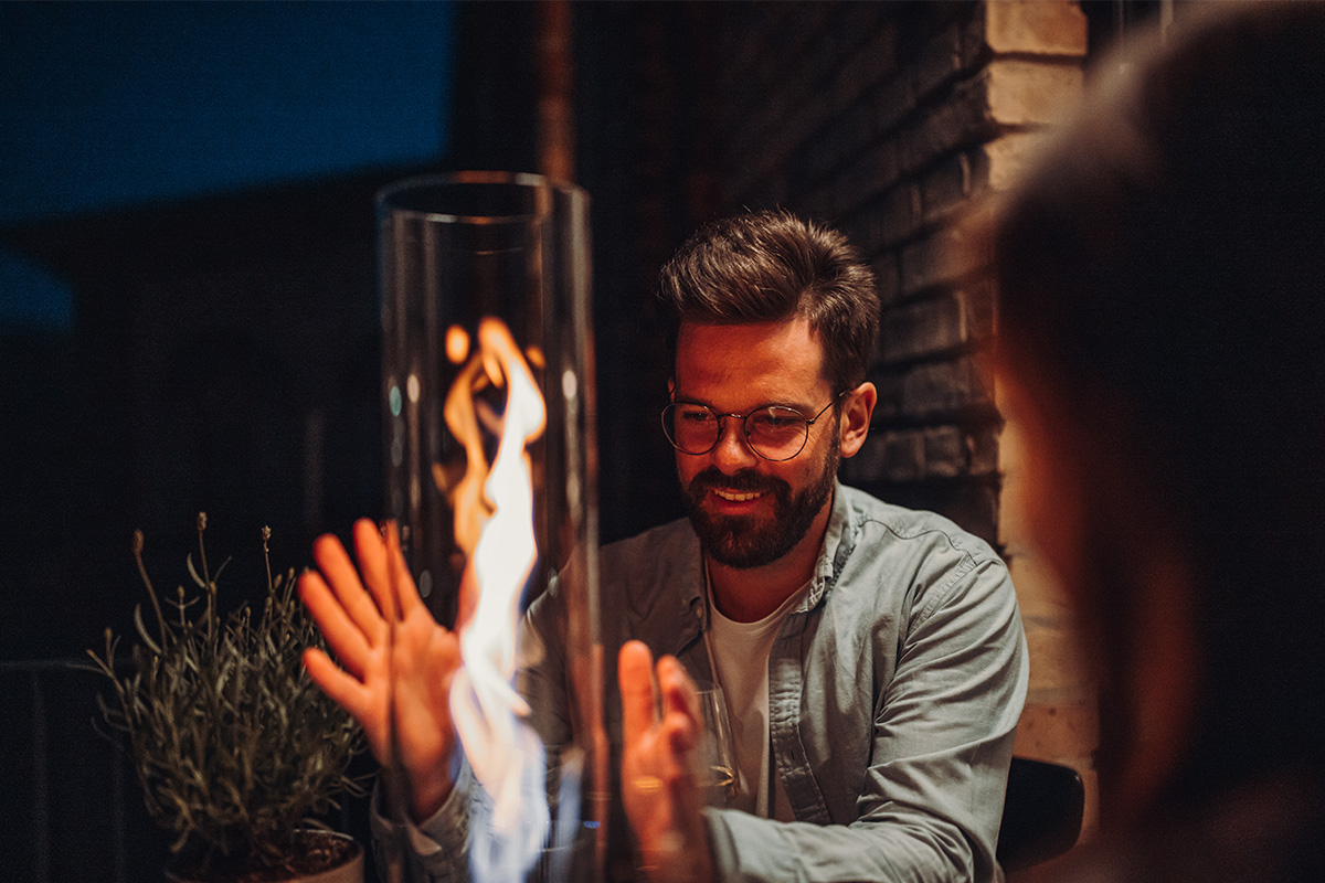 SPIN 90 Tabletop Fireplace silver A depiction of a man is smiling while he looks at a fire, featuring the Spin 90 Tablefire silver as a central and purposeful element.