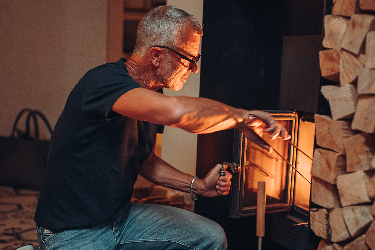Fire Tongs Illustrated is a man is putting a fire in a wood stove, with the Fire Tongs.