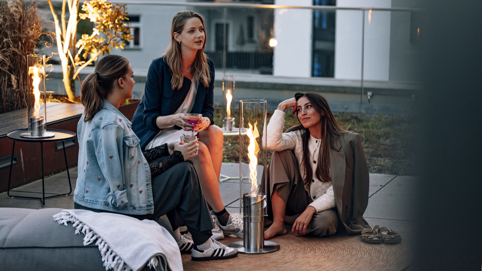 Three women sitting on a couch with a Tablefire, with the 00629 Spin 1500 elevation silver adding a functional and elegant touch to the scene.