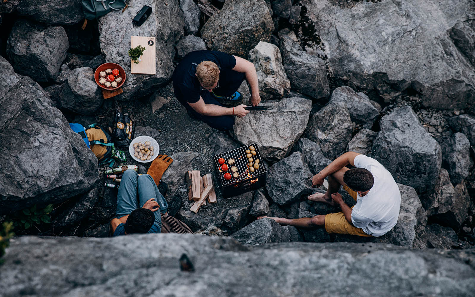 The photo presents a group of people sitting on a rock, with the BEER BOX Fire Basket.