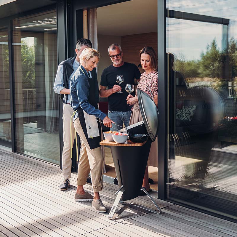 This image shows a man and woman standing on a deck with a grill, with the CONE Charcoal Grill.