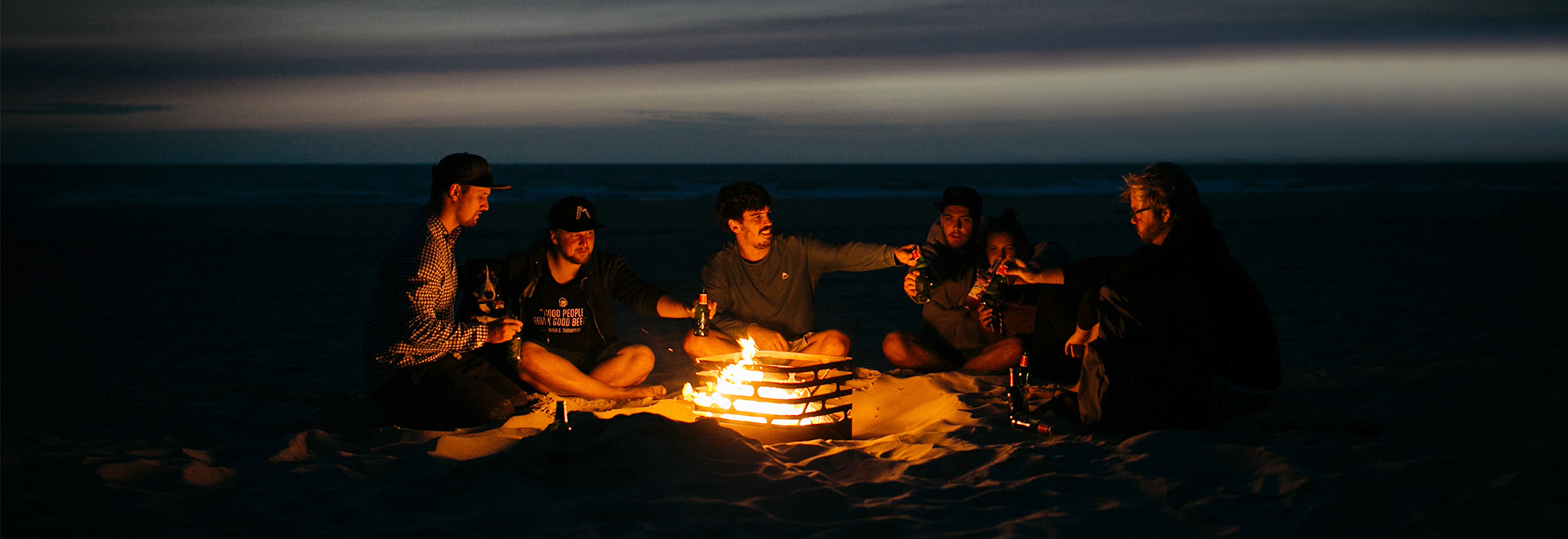 The photo presents a group of people sitting around a fire, with the LOGO SPIN Table-top fireplace.