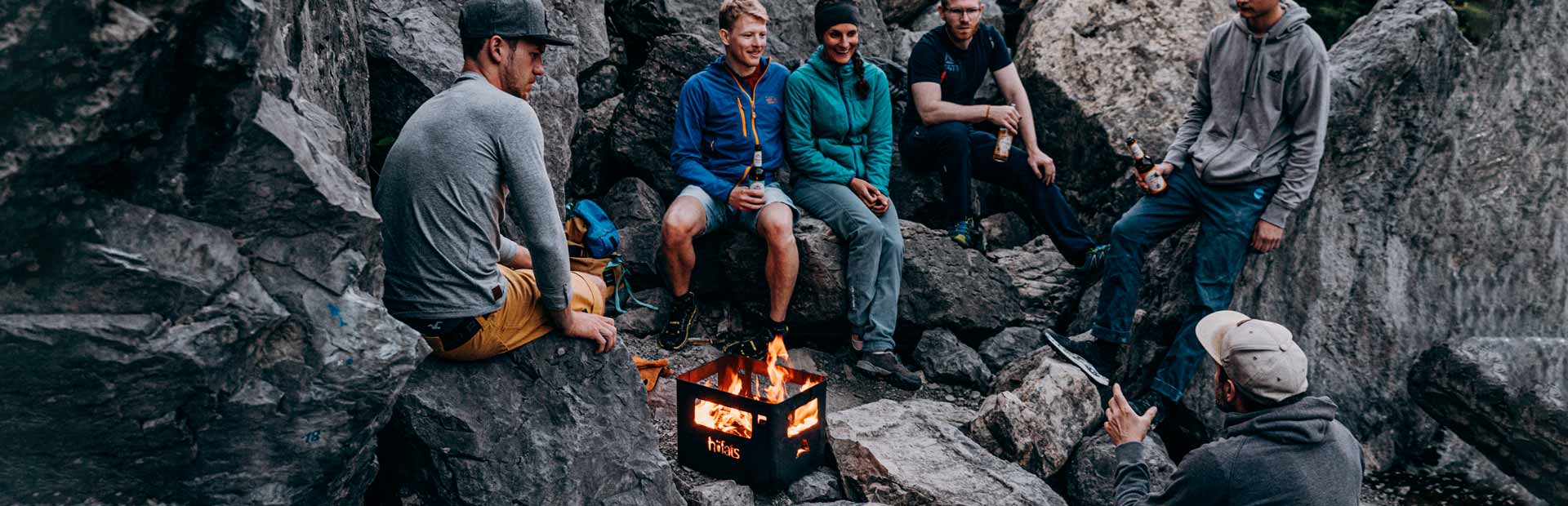 An image showing a group of people sitting around a campfire, with the BEER BOX Fire Basket.