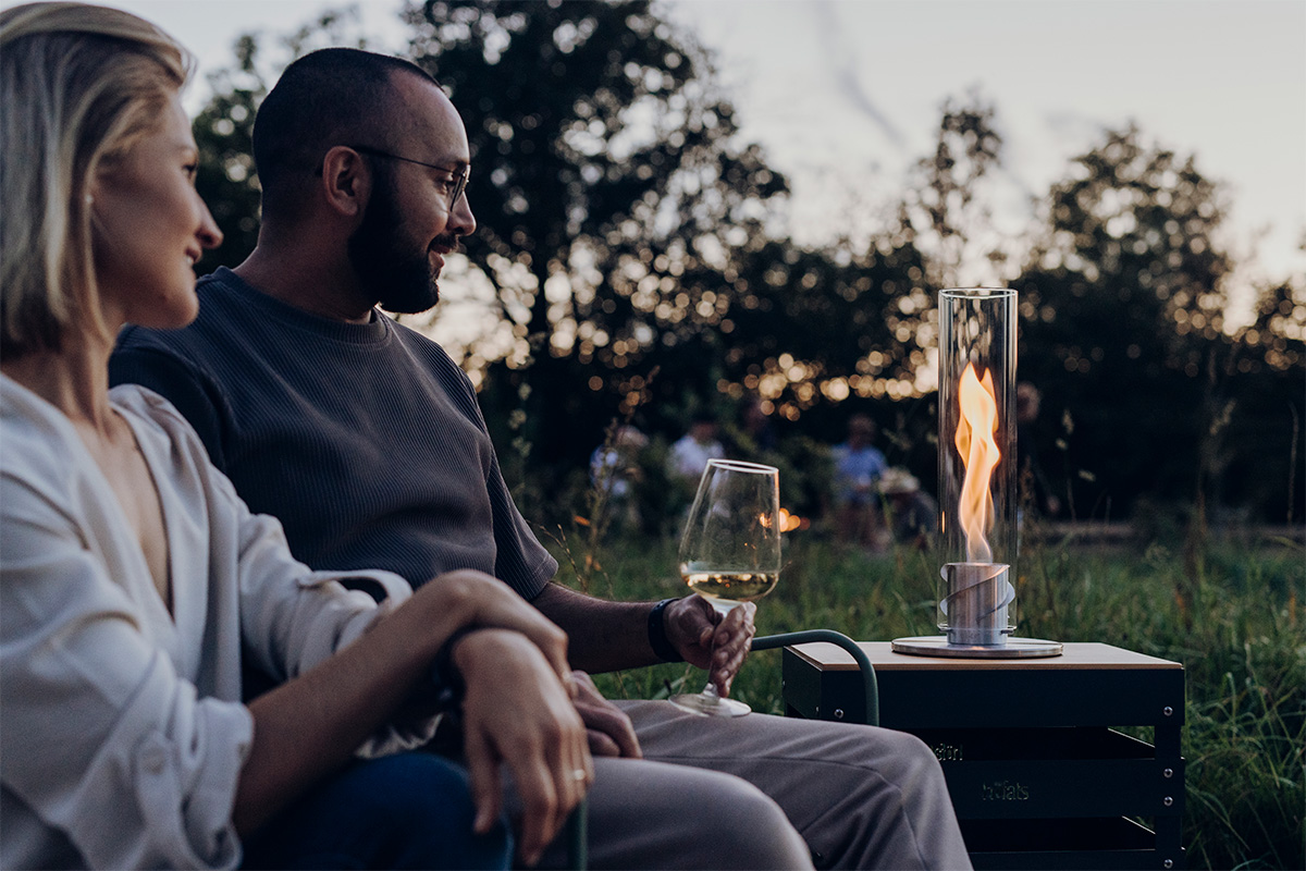 SPIN 900 Tabletop Fireplace silver Depicted here is a man and woman sitting on a bench, with the SPIN 900 Tabletop Fireplace silver.